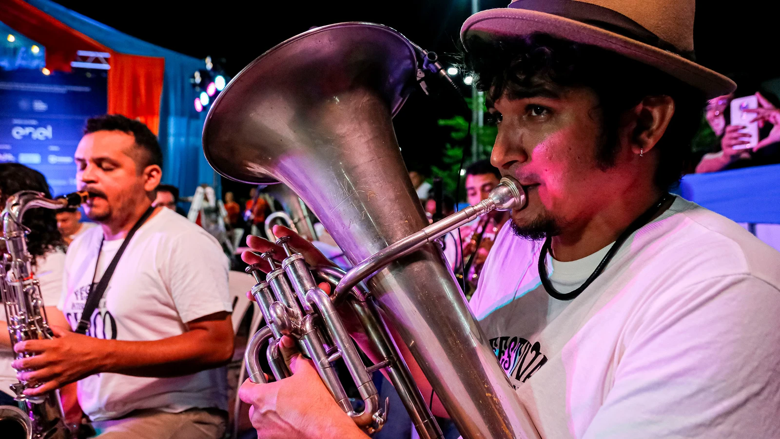 Músicos da Charanga do Festival em apresentação, com instrumentos de sopro e um músico de chapéu em primeiro plano.